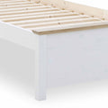 A white wooden bed frame partially shown with slats on top, against a white background.