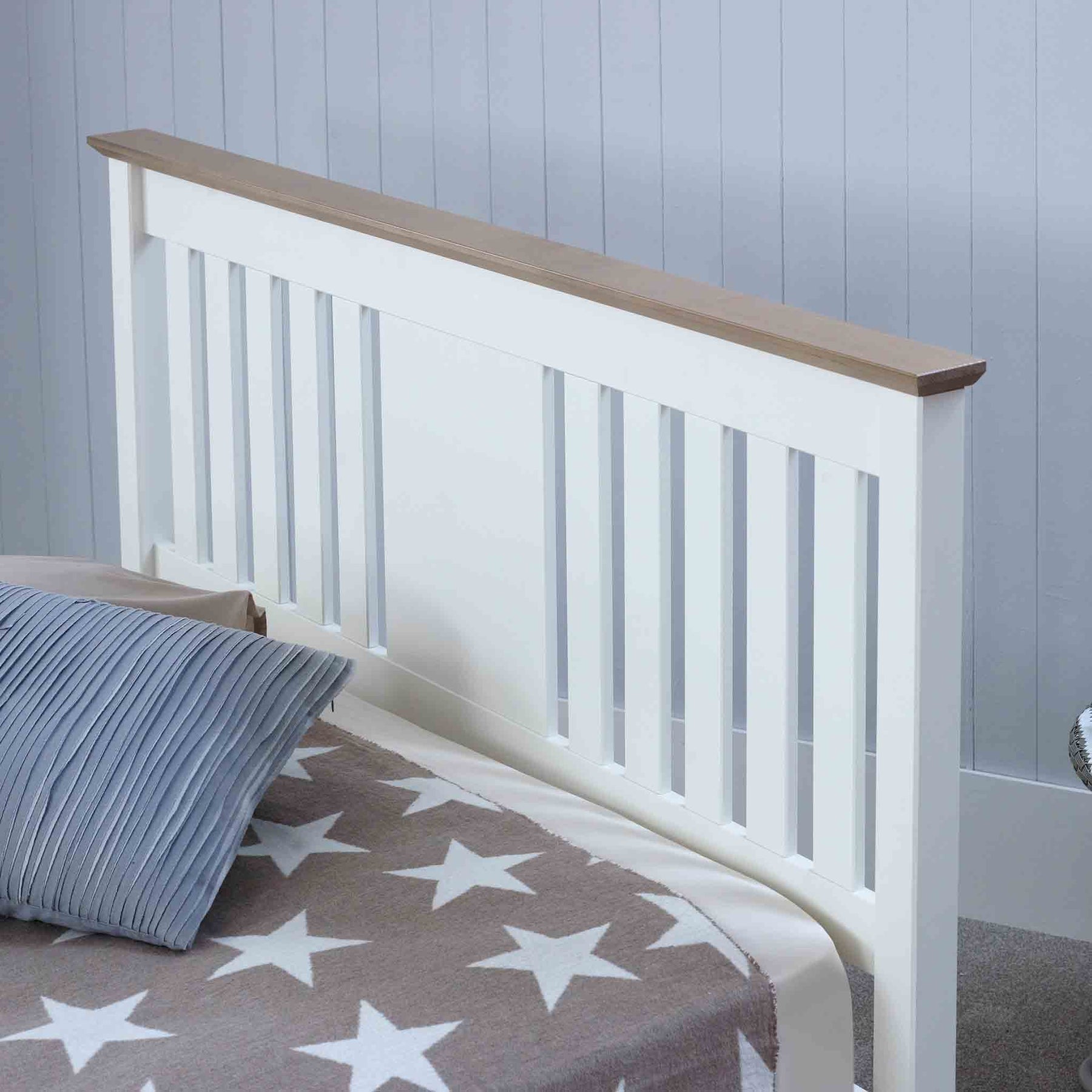 A white bed frame with wooden railings stands against a grey wall, partially covered by a striped pillow and a star-patterned blanket.