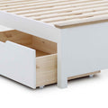 A portion of a white bed frame with a visible wooden slat base and an open storage drawer on wheels, against a white background.