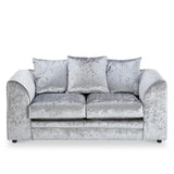 A silver crushed velvet sofa, with two matching cushions, sits idle against a white background, showcasing its plush texture and contemporary design.