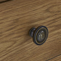 A round, dark-hued drawer knob is mounted on a wood-textured surface, appearing to be part of a furniture piece.