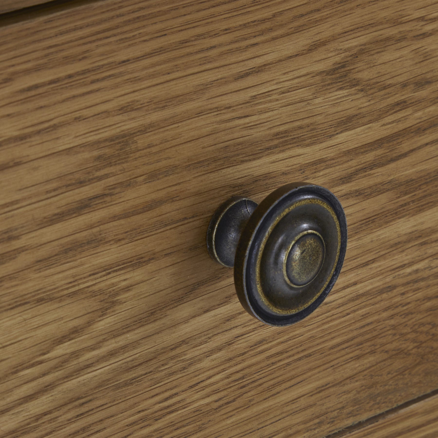 A round, dark-hued drawer knob is mounted on a wood-textured surface, appearing to be part of a furniture piece.