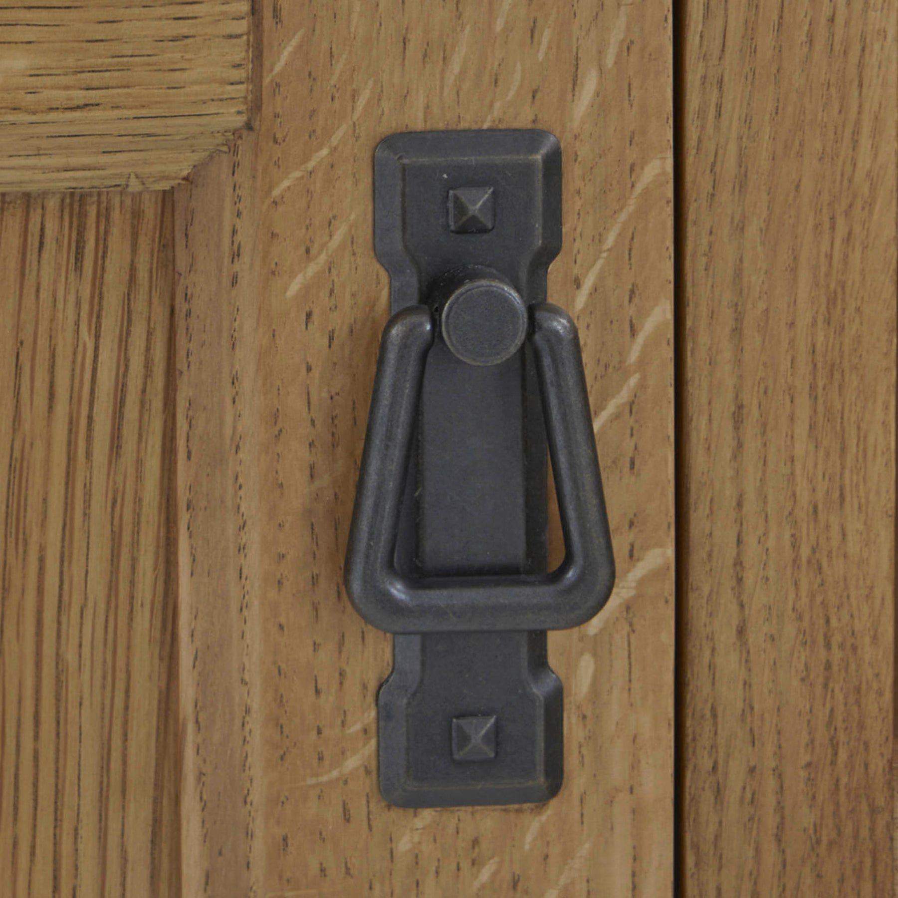 A dark metal door knocker is mounted on a light wooden door, featuring a simple geometric design.