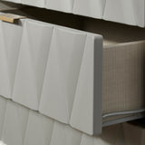 A white textured radiator cover with a geometric pattern, partially obscuring a beige radiator, against a white tiled wall with dark grout.