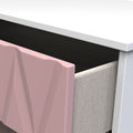 A pink geometric panel leans against a white tabletop, near a gray upholstered chair, suggesting an interior design context.