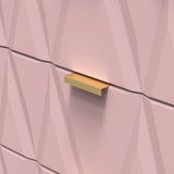 A gold-colored shelf is affixed to a textured pink wall, creating a shadow beneath it.