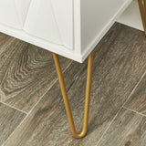A white cabinet with a geometric design and slender, gold-colored metal legs stands on a wooden floor.